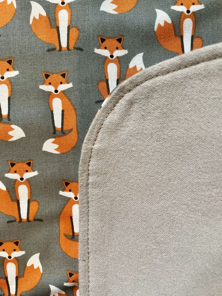 Red foxes adorn the front side of Fabulous Foxes adult bib by BAVETTE while the reverse side is made of soft taupe flannel fabric.