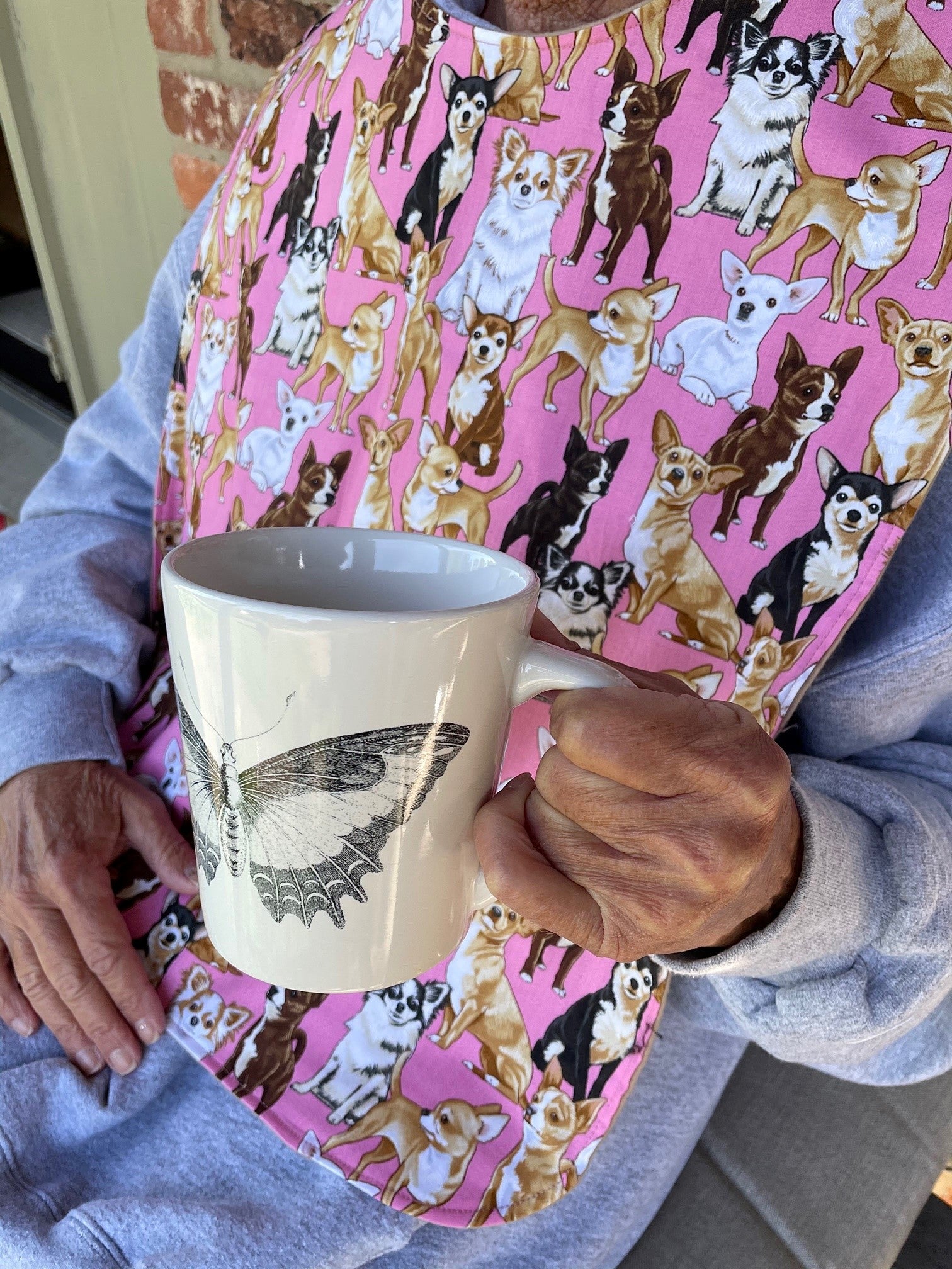 Woman sipping coffee while wearing stylish pink adult bib with dogs to protect clothes
